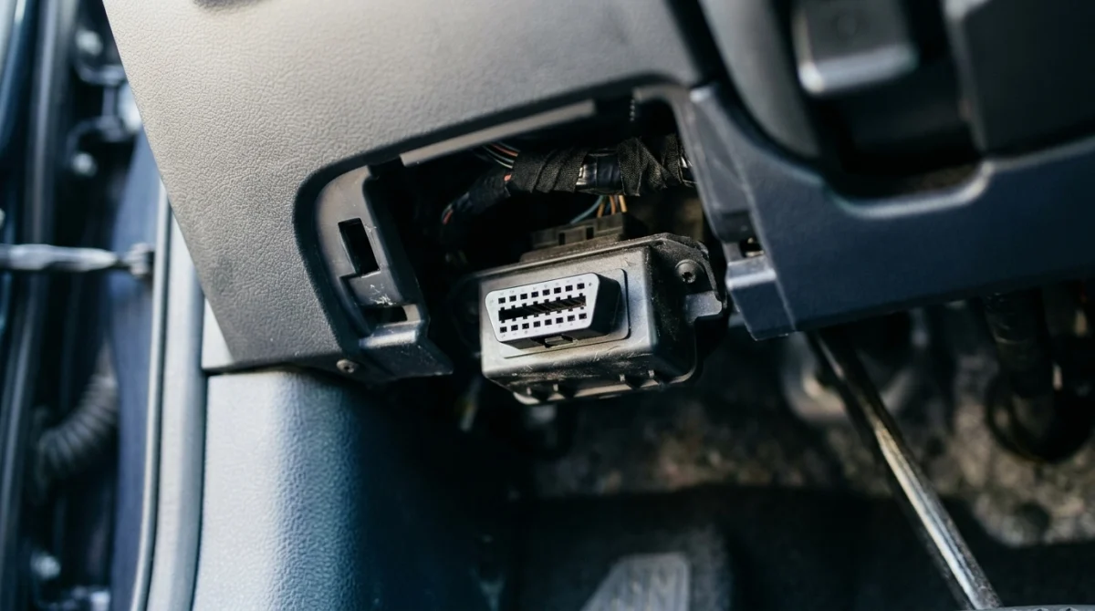 Close-up of a 16-pin OBD2 port mounted beneath a car's dashboard.